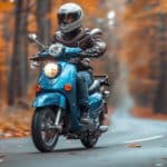 Une Personne Portant Un Casque Et Une Veste En Cuir Conduit Un Scooter Bleu à Travers Une Forêt D'automne Aux Feuilles D'oranger.