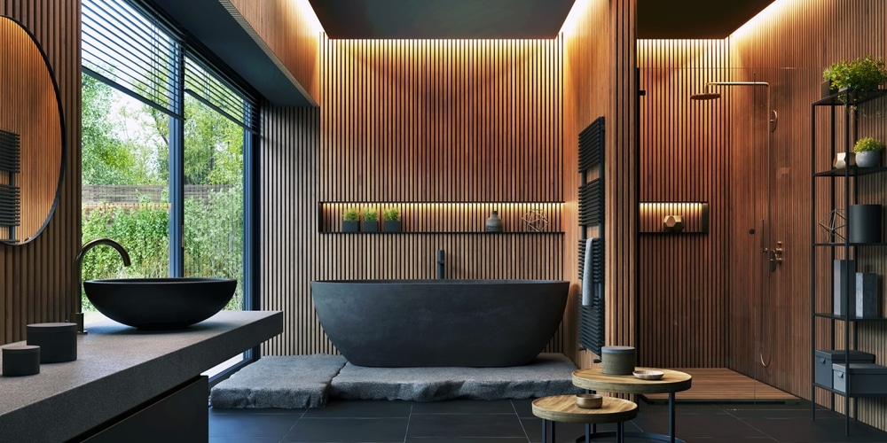 Salle de bains moderne avec boiseries murales, baignoire autoportante noire, miroir circulaire et grandes fenêtres. Cette chambre dispose de plantes d'intérieur, d'un espace douche et d'une décoration minimaliste.