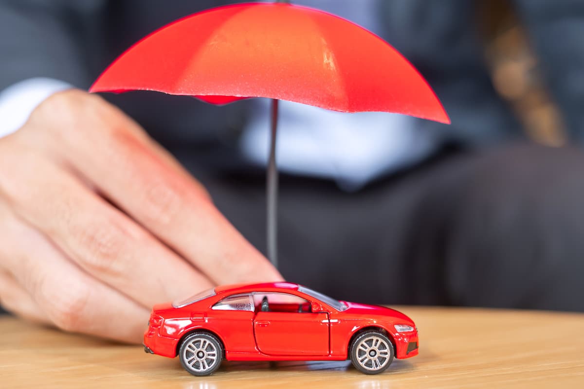 Une personne tient un petit parapluie rouge sur une voiture jouet rouge sur une surface en bois.