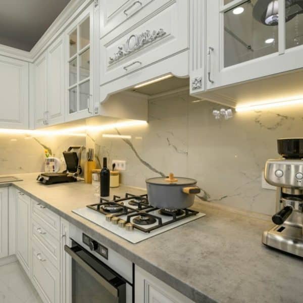 Cuisine Moderne Avec Armoires Blanches, Dosseret En Marbre Et Comptoirs Gris. Comprend Une Cuisinière Avec Une Casserole, Une Machine à Café Et Divers Appareils De Cuisine.