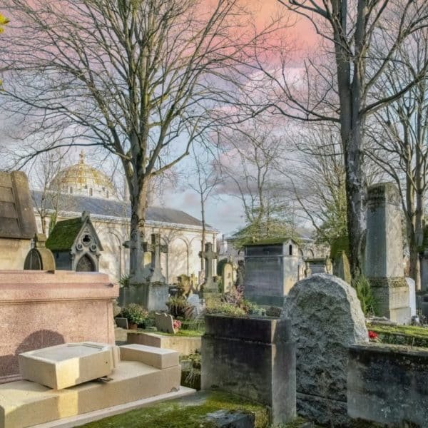 Une Scène De Cimetière Pittoresque Avec Des Pierres Tombales, Des Arbres Nus Et Un Bâtiment En Forme De Dôme En Arrière Plan Sous Un Ciel Coloré.