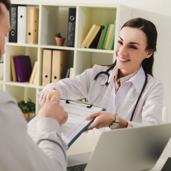 smiling doctor showing insurance claim form to client in office, life insurance concept