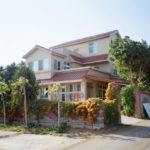 Maison à Deux étages Avec Un Toit De Tuiles Rouges, Entourée D'une Clôture Recouverte De Verdure Et De Fleurs Oranges, Située à L'intersection De Deux Routes Par Temps Clair.