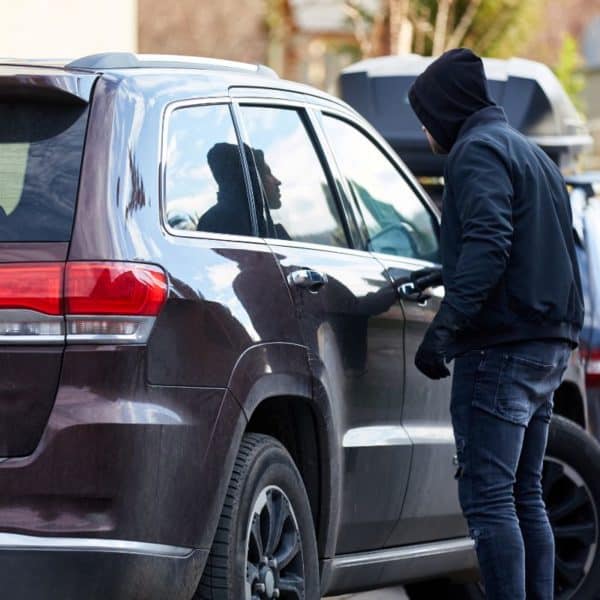 Une Personne Portant Un Sweat à Capuche Se Tient à Côté D'un Suv Sombre, Regardant à Travers La Fenêtre Côté Conducteur Du Véhicule à L'abri Du Vol étonnamment Sécurisé, Avec Une Autre Voiture Garée à Proximité.