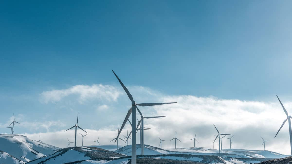 Des éoliennes Sur Des Collines Enneigées Sous Un Ciel Bleu Clair, Générant De L'énergie Renouvelable.