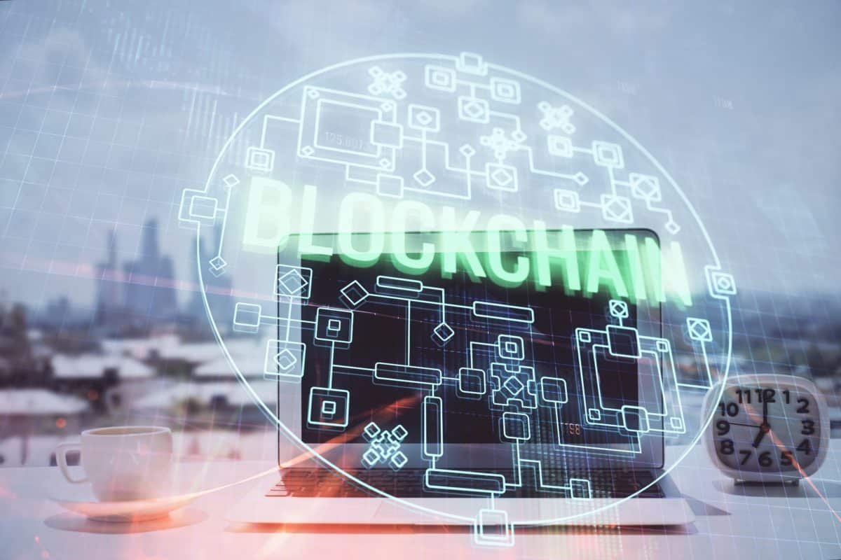 Un Ordinateur Portable Posé Sur Un Bureau Affiche Des Graphiques Numériques De Blockchain, Avec Le Mot « blockchain » Et Des Icônes En Forme De Circuit Superposés. Une Tasse à Café, Un Carnet Et Une Horloge Sont également Visibles.