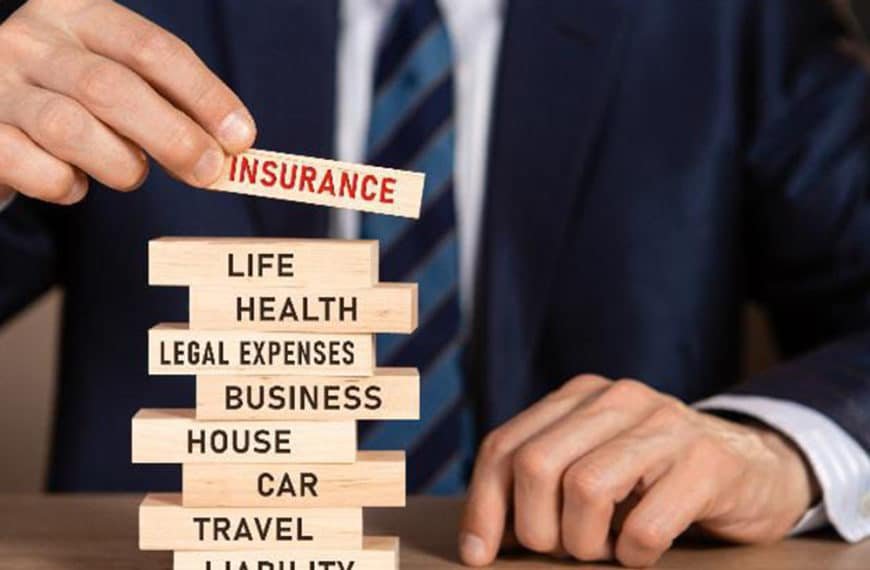 Une Personne En Costume Place Un Bloc De Bois étiqueté "assurance" Au Dessus D'une Pile De Blocs étiquetés Avec Des Catégories Telles Que Vie, Santé, Maison, Voiture, Voyage Et Responsabilité.