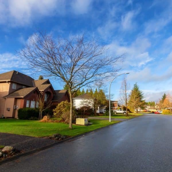 Rue de quartier de banlieue avec des maisons unifamiliales, des arbres sans feuilles, des pelouses et un ciel partiellement nuageux par temps clair.