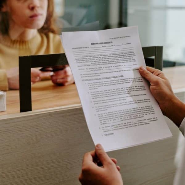 Une Personne Remet Un Document à Une Femme Debout à Un Comptoir De Service, Qui Tient Sa Carte D'identité.