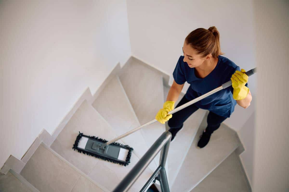 Une Femme Portant Des Gants Et Une Chemise Bleue Nettoie Un Escalier Avec Une Serpillière Plate.
