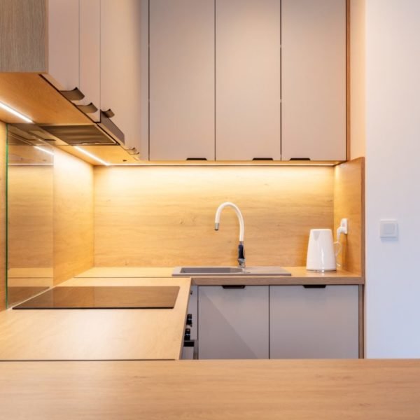 Cuisine Moderne Avec Des Meubles En Bois Et Beige, Un éclairage Sous L'armoire, Une Table De Cuisson électrique, Un évier Et Une Bouilloire électrique Blanche Sur Le Comptoir.