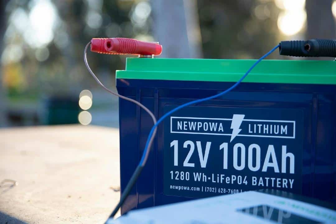 Gros Plan D'une Batterie Au Lithium Newpowa 12v 100ah Avec Ses Câbles Rouge Et Noir, Placée à L'extérieur Sur Une Surface.