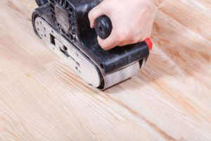 Une Personne Utilise Une Ponceuse à Bande Manuelle Pour Lisser La Surface D'un Plancher En Bois.