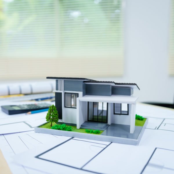 La Maquette D'une Maison Moderne Est Posée Sur Des Plans D'architecte Sur Un Bureau, Avec Une Calculatrice Et Une Chaise De Bureau à L'arrière Plan.