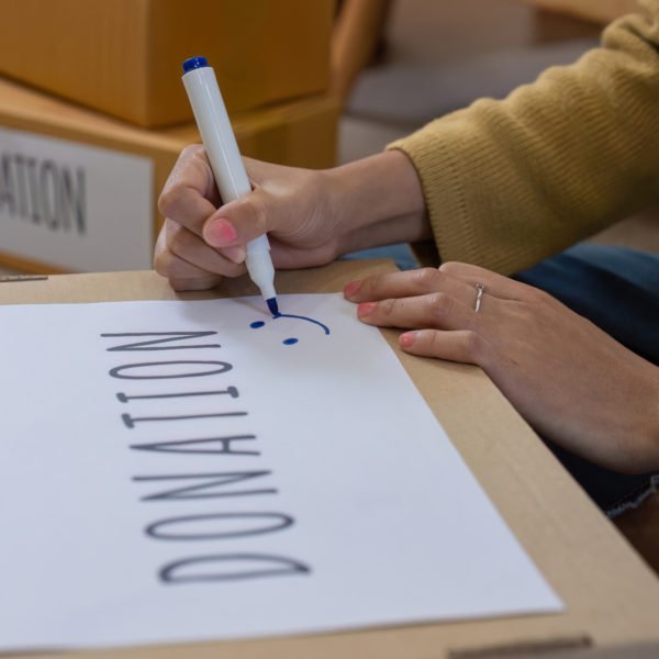 Une Personne écrit Au Marqueur Sur Une Boîte En Carton Portant L'inscription "don". D'autres Boîtes Portant Des étiquettes Similaires Se Trouvent à L'arrière Plan.