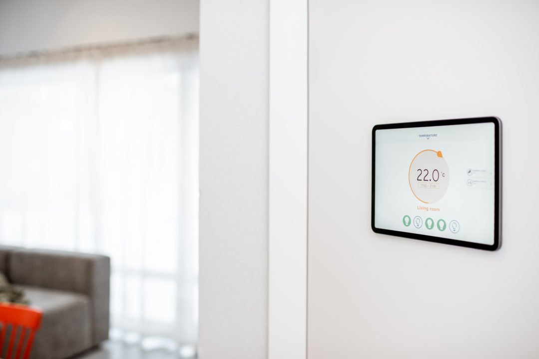 Un Thermostat Numérique Monté Sur Un Mur Blanc Affiche Une Température Ambiante De 22,0°c Dans Un Salon Moderne Et Lumineux.