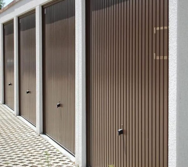 Une Rangée De Portes De Garage Brunes Fermées Avec Un Trottoir à Motifs Devant, Idéal Pour Ceux Qui Recherchent Une Solution Garde Meuble Sécurisé Angers.