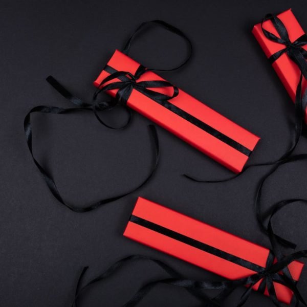 Quatre Boîtes Rectangulaires Rouges Avec Des Rubans Noirs Sont Disposées Sur Une Surface Noire, Avec Quelques Brins De Rubans Enroulés Autour Des Boîtes.