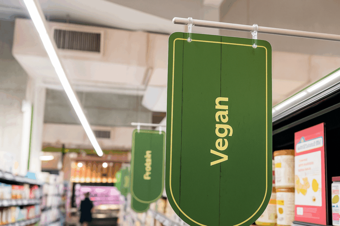 Un Panneau Vert De L'épicerie Portant Le Mot "vegan" Est Suspendu Au Dessus D'une Allée, Indiquant La Section Réservée Aux Produits Végétaliens.