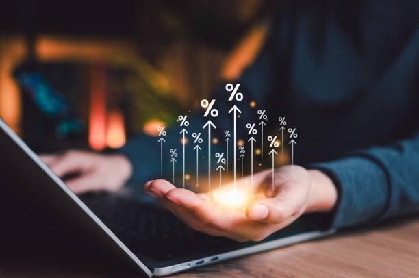 Une Personne Tient Au Dessus De Sa Paume Un Affichage Lumineux De Symboles De Pourcentages Croissants, Avec Un Clavier D'ordinateur Portable Visible En Arrière Plan.