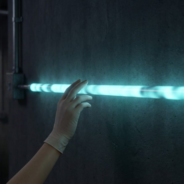 Une main gantée touche un tube néon bleu-vert vibrant ou clignotant, fixé à un mur sombre. Ambiance de laboratoire.