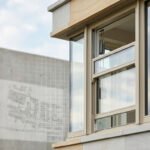 Fenêtre à guillotine moderne partiellement ouverte sur une façade de bâtiment clair. Plans d'architecture en arrière-plan flou.