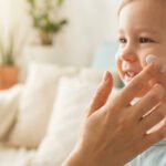 Gros plan: main appliquant de la crème sur la joue souriante d'un jeune enfant. Image douce évoquant les soins pour bébé.