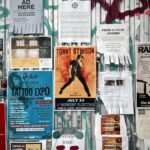 Un Mur Couvert D'affiches Et De Prospectus Pour Des Concerts, Des Expositions De Tatouages, Des Cours De Musique Et Des événements Communautaires, Le Tout Attaché à Une Clôture Métallique Ornée De Graffitis.