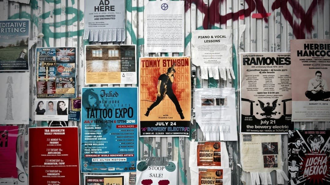 Un Mur Couvert D'affiches Et De Prospectus Pour Des Concerts, Des Expositions De Tatouages, Des Cours De Musique Et Des événements Communautaires, Le Tout Attaché à Une Clôture Métallique Ornée De Graffitis.