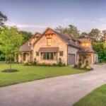 Une Grande Maison En Pierre à Deux étages Avec Une Pelouse Bien Entretenue, Une Allée Incurvée Et Des Arbres Entourant La Propriété Au Coucher Du Soleil.