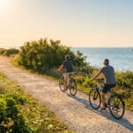 Deux personnes à vélo sur un chemin côtier de l'Île d'Aix au coucher du soleil, avec la mer et un ferry.