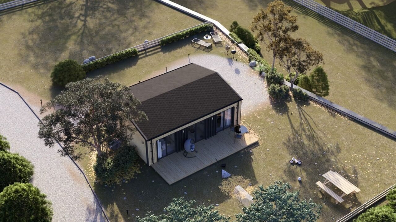 Une Petite Maison Moderne Avec Un Toit Sombre, Une Terrasse En Bois Et Des Sièges Extérieurs, Entourée D'arbres, De Buissons Et D'un Chemin De Gravier à L'intérieur D'une Cour Herbeuse Clôturée.