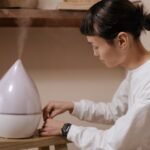 Une Personne En Chemise Blanche Règle Un Humidificateur émettant De La Brume Sur Une Surface En Bois à L'intérieur.
