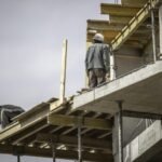 Deux Ouvriers De La Construction Portant Des Casques De Sécurité Travaillent Sur Une Structure De Bâtiment à Plusieurs étages, En Manipulant Des Planches De Bois Et Des échafaudages.