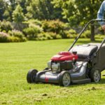 Un homme en chemise bleue et pantalon beige se tient à côté d'une tondeuse Honda HRX 537 noire et rouge sur une pelouse verte.